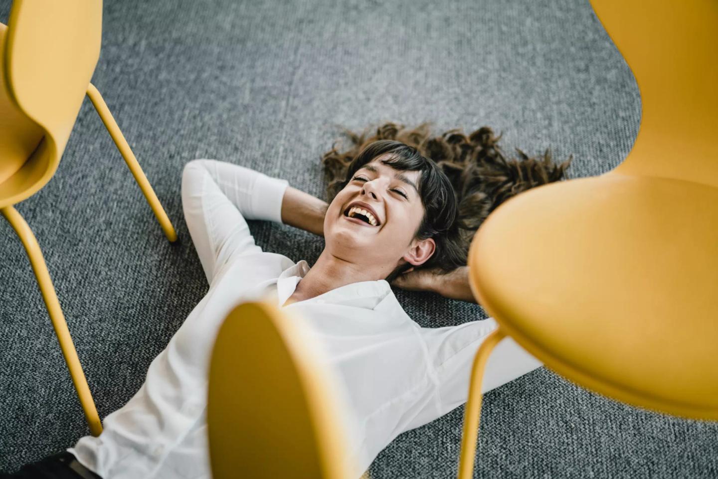 Person ligger avslappet og leende på gulvet i et konferanselokale.