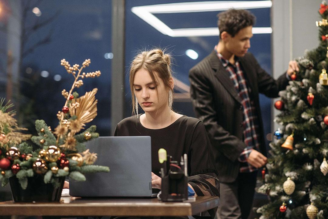 Dame som sitter og jobber på datamaskin med juletre i bakgrunnen
