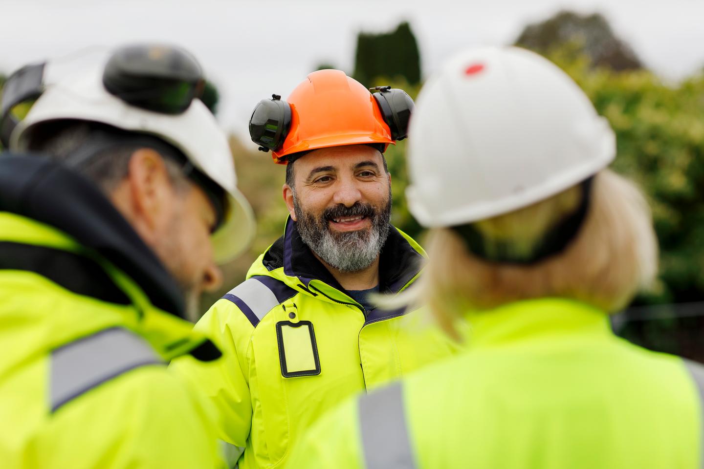 Tre bygg- eller anleggsarbeidere med verneutstyr som snakker sammen