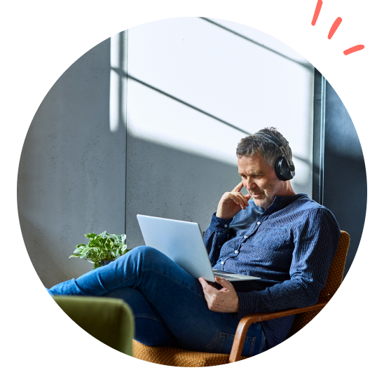 Mann sitter i stol med laptop og hodetelefoner på hjemmekontor, illustrerer ergonomi ved hjemmearbeid.