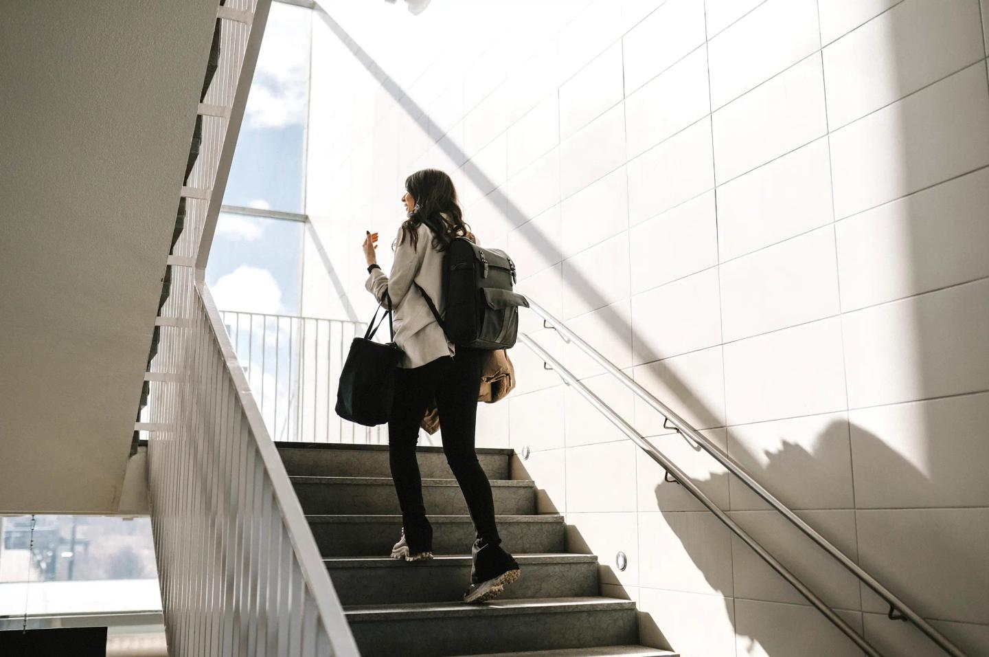 Person på jobbreise går opp en trapp i et solfylt innendørs trappehus.